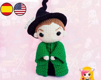 May include: Crocheted amigurumi doll of a young wizard wearing a black pointed hat and a green robe. The doll has brown hair, a white face, and black eyes. The doll is standing on a pink background with a pattern of hearts and stars.