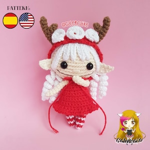 Op de afbeelding: Een gehaakte elfpop die een rode jurk en een witte capuchon met bruine geweien draagt. De pop heeft wit haar en zwarte ogen. De pop houdt haar handen voor haar borst bij elkaar. De pop staat op een roze achtergrond. De tekst "@calencaixe" staat op de achtergrond.