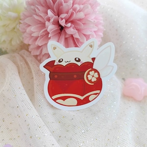 Puede incluir: Una pegatina de dibujos animados blanca y roja de una pequeña criatura blanca similar a un conejo con orejas grandes y una bolsa roja en forma de corazón. La criatura lleva una faja roja y marrón y tiene un ala blanca pequeña en la espalda. La pegatina está sobre un fondo blanco brillante.