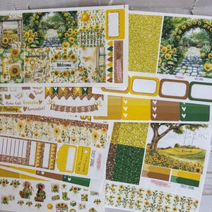 May include: A collection of decorative planner stickers with a sunflower theme. The stickers feature images of sunflowers, garden scenes, and the text "Welcome" and "Weekend". The color palette includes yellow, green, and brown.