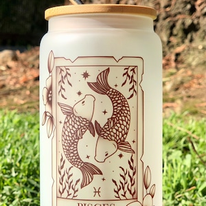 Vaso de vidrio esmerilado con tapa de bambú y pajita, con la carta del tarot del zodíaco Piscis