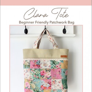 Peut inclure: Un sac cabas en patchwork avec un tissu floral dans des tons de rose, vert et jaune. Le sac a une base en toile beige et une étiquette en cuir marron qui dit "Clara Tote". Le sac est accroché à un mur blanc avec des crochets noirs. Le texte "Beginner Friendly Patchwork Bag" est au-dessus du sac. Le texte "Molly and Mama STUDIO for PRETTY STITCHES" est en dessous du sac.