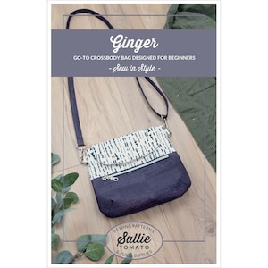 May include: A navy blue crossbody bag with a flap closure and a patterned top section. The bag has a silver zipper and a long, adjustable strap. The text "Ginger" and "Sew in Style" are visible. The bag is designed for beginners.