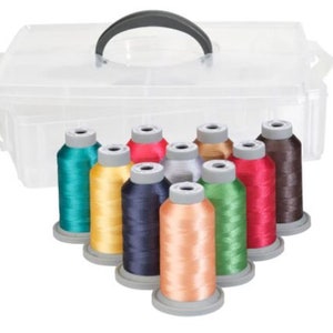 Op de afbeelding: Een doorzichtige plastic opbergdoos met een zwarte handgreep, met spoelen van kleurrijk borduurgaren. De draadkleuren zijn onder meer turquoise, geel, marineblauw, perzik, zilver, bruin, rood en groen.