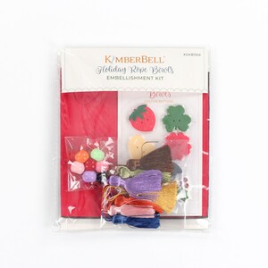 May include: A package containing a Kimberbell Holiday Rope Bowls Embellishment Kit. The kit includes a variety of colorful buttons, beads, and tassels. The package also includes a red cardstock sheet and a sheet of instructions.