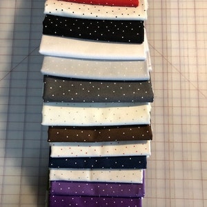 Pode incluir: Uma pilha de 12 quadrados de tecido com bolinhas brancas em fundos de cores diferentes. As cores incluem vermelho, preto, branco, cinza, marrom, azul marinho, roxo e verde.