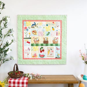 May include: A patchwork quilt with a picnic theme, featuring squares with images of baskets, fruit, and flowers. The quilt has a green dotted border and a pink inner border. The text "Sippin' on Sunshine" is visible.