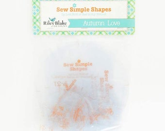 May include: A clear plastic bag with a white background containing a set of orange fabric shapes. The bag has a label that reads "Sew Simple Shapes by Lori Holt of Bee in my Bonnet Riley Blake Designs Autumn Love".