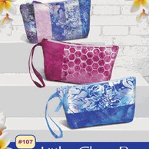 May include: Three colorful zippered pouches with handles. The pouches are made with fabric featuring different patterns. The pouches are labeled "Little Glam Bag" and "#107".