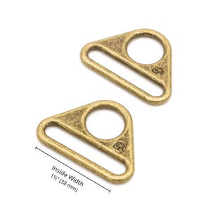 Puede incluir: Dos anillos en D de metal de forma triangular de color dorado antiguo con una anchura interior de 38 mm (1 1/2 pulgadas).