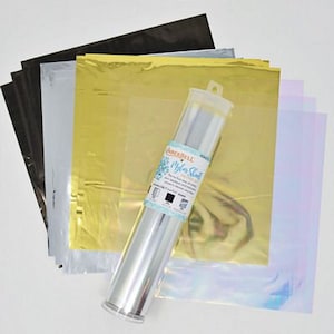 May include: A roll of silver adhesive backed mylar sheets for crafting. The roll is labelled "Scor-Pal Myla-Stix" and is next to a stack of iridescent, gold, silver, and black sheets.