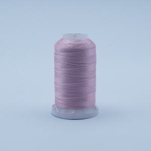 May include: A spool of pale pink thread, tightly wound around a white plastic core. The thread has a subtle sheen, suggesting a smooth, high-quality material. Ideal for sewing, embroidery, or other textile crafts.