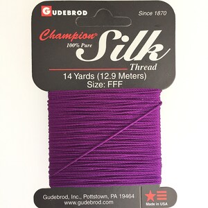 May include: A spool of deep purple Champion Silk Thread. The label states "100% Pure Silk Thread" and "14 Yards (11.89 metres)". The packaging is black with white text, and the brand name "GUDEBROD" is at the top.