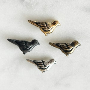May include: Four small metal bird figurines in different finishes: gold, silver, and black. The birds are all facing the right side of the image.