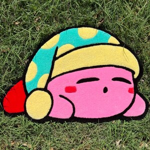 May include: A pink and blue plush rug shaped like a sleeping cartoon character wearing a blue and yellow hat.