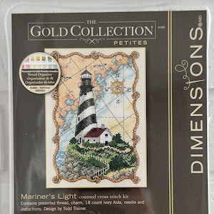 May include: A cross-stitch kit titled "Mariner's Light" from The Gold Collection Petites. The kit features a lighthouse scene with a black and white striped tower, a small white building, and a map background. The package measures 5 x 7 inches.