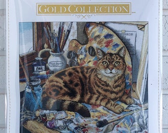 May include: A counted cross stitch kit featuring a cat sitting on a paint-splattered canvas with paintbrushes, a palette, and paint tubes. The kit is titled "Leonardo" and includes the dimensions 14 inches by 12 inches (35.5 cm x 30.4 cm).