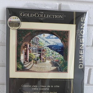 Puede incluir: Kit de punto de cruz Dimensions Gold Collection, titulado "Coastal View". Presenta una imagen detallada de un pueblo costero con un arco de piedra y vistas al mar. El kit mide 38,1 cm por 30,4 cm.