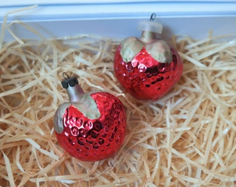 May include: Two red glass Christmas baubles with a textured surface, nestled in shredded paper inside a white gift box.