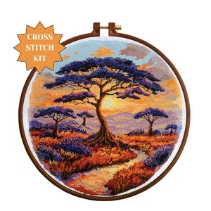 May include: A cross stitch kit featuring a sunset landscape with a large tree in the center and smaller trees in the foreground. The sky is a gradient of orange, pink, and purple. The trees are a dark purple color. The kit includes all the materials needed to complete the cross stitch project.