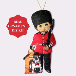 May include: A decorative ornament featuring a cartoon depiction of a British Royal Guard in a red coat and black hat, holding a rifle. The ornament includes a picture of a bulldog and the text "BEAD ORNAMENT DIY KIT".