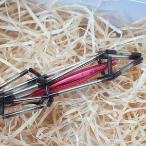 May include: A red and silver glass Christmas ornament shaped like a rocket ship. The ornament is made of glass tubes and is decorated with silver paint.
