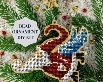 May include: A wooden Christmas ornament shaped like a Santa Claus with a blue and white wing. The ornament is covered in colorful beads and is part of a DIY bead kit.