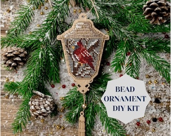 May include: A wooden Christmas ornament shaped like a lantern with a red cardinal bird inside. The ornament is decorated with beads and comes with a tassel. The ornament is part of a bead ornament DIY kit.