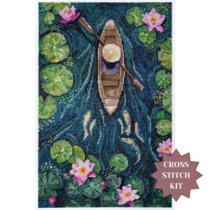 Op de afbeelding: Kruissteekpakket met een serene scène van een boot op een vijver. De afbeelding toont een houten boot met een persoon met een hoed, omringd door waterlelies, roze lotusbloemen en vissen. Het water is diepblauw, met de tekst 'CROSS STITCH KIT'.