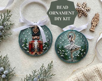 May include: Two circular ornaments featuring beadwork designs of a nutcracker and a ballerina on a green background. Each ornament has a white ribbon loop. A wooden snowflake and nutcracker figure are included in this bead ornament DIY kit.