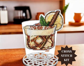 May include: A cross-stitch kit featuring a cocktail design. The drink is in a clear glass with ice cubes, a lemon slice, mint, and a cinnamon stick. The kit includes a decorative coaster. The text "CROSS STITCH KIT" is on the image.