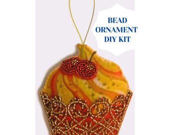 May include: A cupcake-shaped bead ornament DIY kit. The ornament features a yellow and orange frosted top with two red beaded cherries. The red beaded cupcake liner is detailed with gold accents. The text "BEAD ORNAMENT DIY KIT" is in blue.