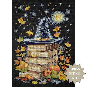 May include: A cross-stitch kit featuring a witch's hat atop a stack of books, surrounded by pumpkins and autumn leaves. The background is a starry night with a full moon. The words "CROSS STITCH KIT" are in a starburst.