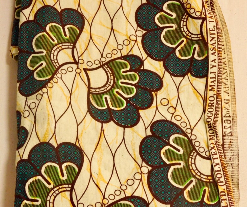 May include: A white fabric with a brown and green floral pattern. The fabric has a brown border with the text "LTD. POLYTEX MOROGORO. MALI YA ASANTE TANZANIA" printed on it.
