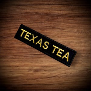 May include: Black fabric patch with yellow embroidered text that reads "TEXAS TEA".