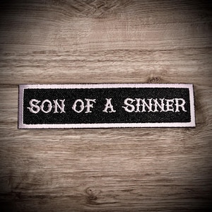 May include: Black and white embroidered patch with the text "Son of a Sinner" in white lettering on a black background. The patch has a white border.