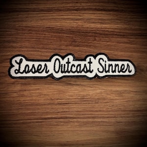 May include: White embroidered patch with black stitching. The patch reads "Loser Outcast Sinner".