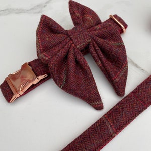 Pode incluir: Uma coleira de tweed bordô para cães com uma gravata borboleta combinando. A coleira tem uma fivela de ouro rosa e a gravata borboleta é amarrada com um laço.