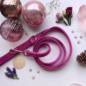 May include: A pink velvet dog leash with a gold clasp and a rose gold charm with the text "Hunter & Co. Dog Collars". The leash is coiled on a white surface with pink and gold ornaments and stars.