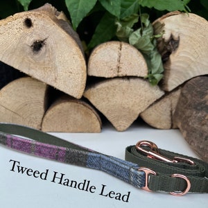 May include: A green dog leash with a tweed handle and a rose gold clasp. The leash is lying on a white surface with a stack of wood behind it. The text "Tweed Handle Lead" is written below the leash.