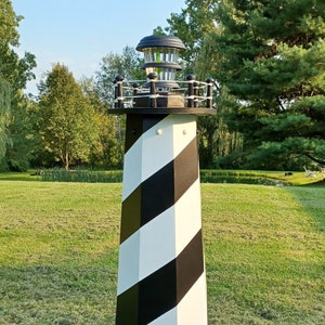 May include: A black and white striped lighthouse with a red base. The lighthouse has a solar powered light on top and is made of wood.