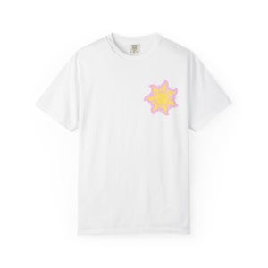 May include: White t-shirt with a yellow sun design and a pink outline on the front. The sun graphic is on the chest. The shirt has a crew neck and short sleeves. The material is soft.