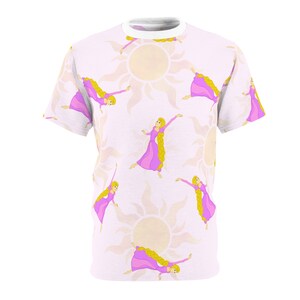 May include: A white t-shirt with a repeating pattern of a cartoon princess with long blonde hair wearing a pink dress and a yellow sun with rays.