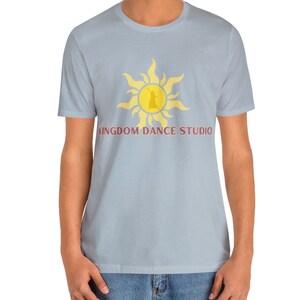 May include: Light blue t-shirt with a yellow sun graphic and a silhouette of a dancer inside. The text "KINGDOM DANCE STUDIO" is printed in purple below the graphic.