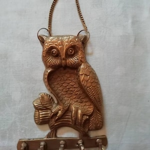 May include: A brass owl key holder with five hooks. The owl is perched on a branch and has a chain for hanging.