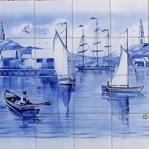 Puede incluir: Un azulejo azul y blanco que representa un paisaje marítimo con veleros y un pequeño pueblo en el fondo.