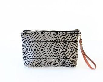 May include: A gray and black zippered pouch with a chevron pattern and a brown leather strap.