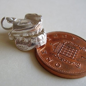 May include: Silver charm in the shape of a saddle, with a loop for attaching to a bracelet or necklace. The charm is shown next to a British one pence coin.