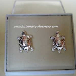 May include: A pair of silver turtle stud earrings in a white box. The earrings are small and detailed, with a textured shell and four legs.