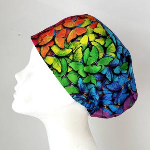 Könnte beinhalten: Eine bunte OP-Mütze mit einem Regenbogenmuster aus Schmetterlingen. Die Mütze ist aus einem weichen, bequemen Stoff gefertigt und perfekt für Krankenschwestern, Ärzte und andere medizinische Fachkräfte.